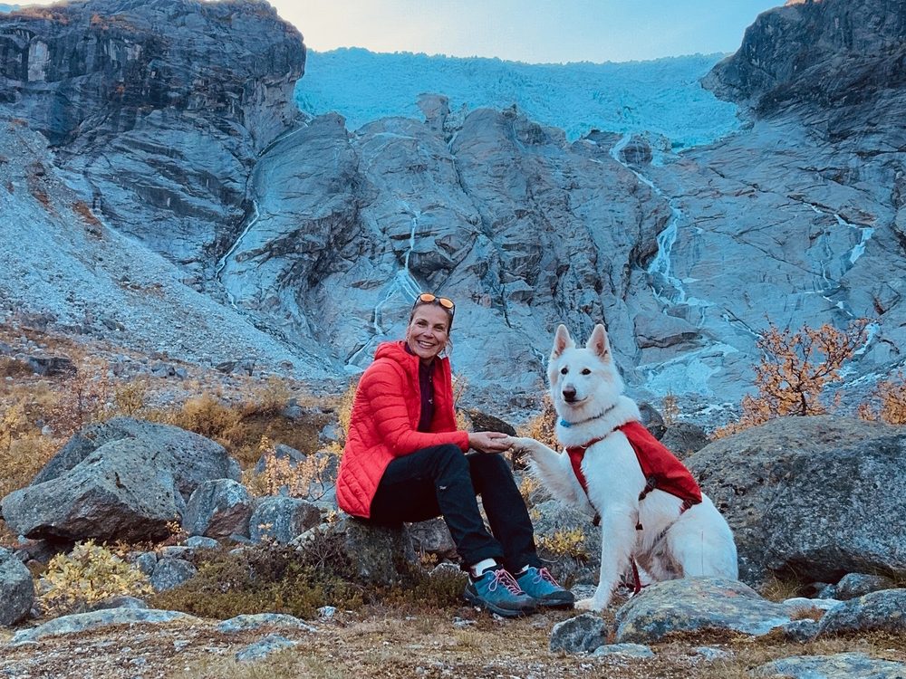 Franziska von Bredow sitzt mit Kuri vor einer Gletscherlandschaft und gibt ihm die Pfote